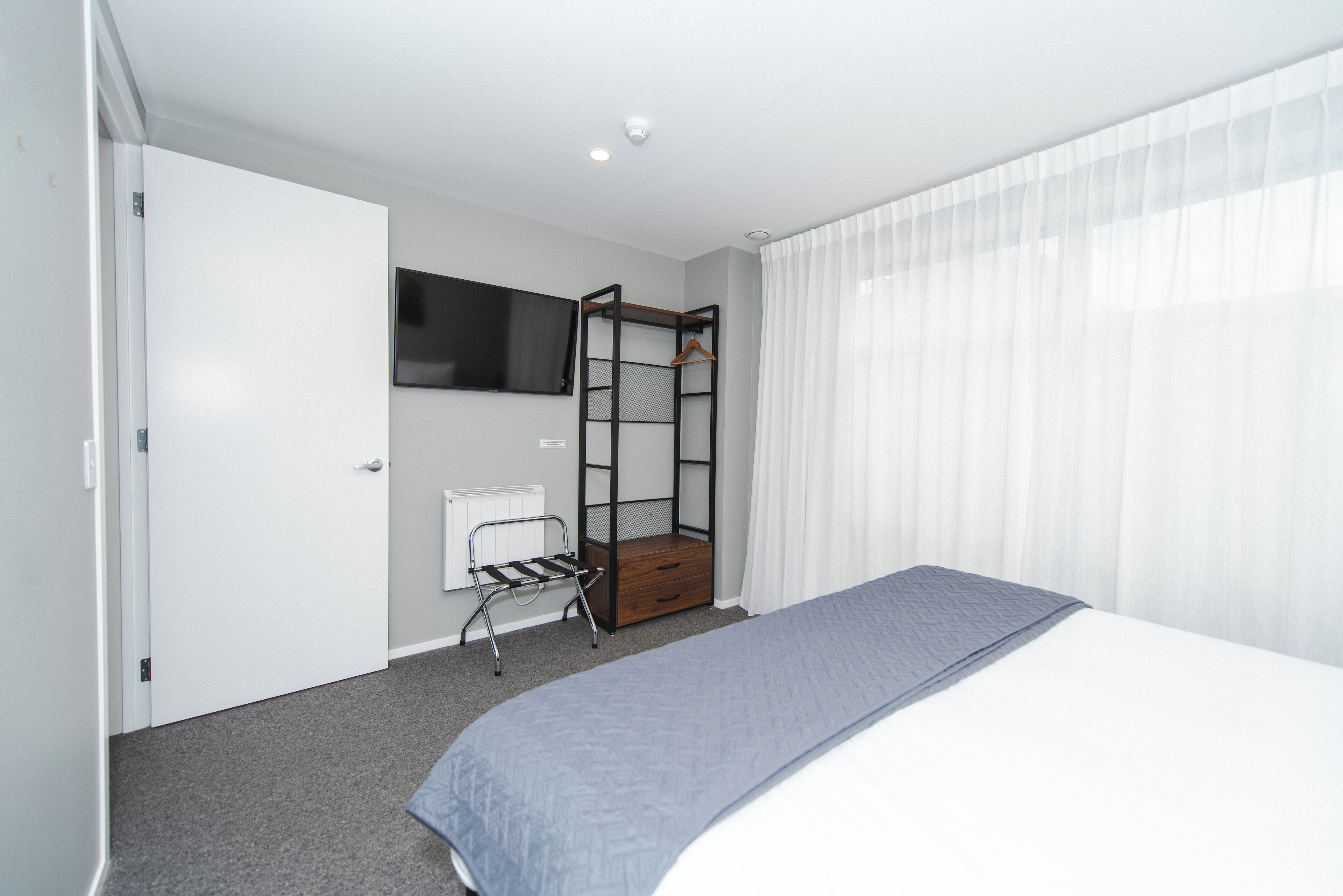 A hotel room with a bed, a TV mounted on the wall, a wooden wardrobe, and a radiator.