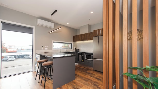 A modern kitchen with a central island, wooden cabinets, and a view through the glass door.
