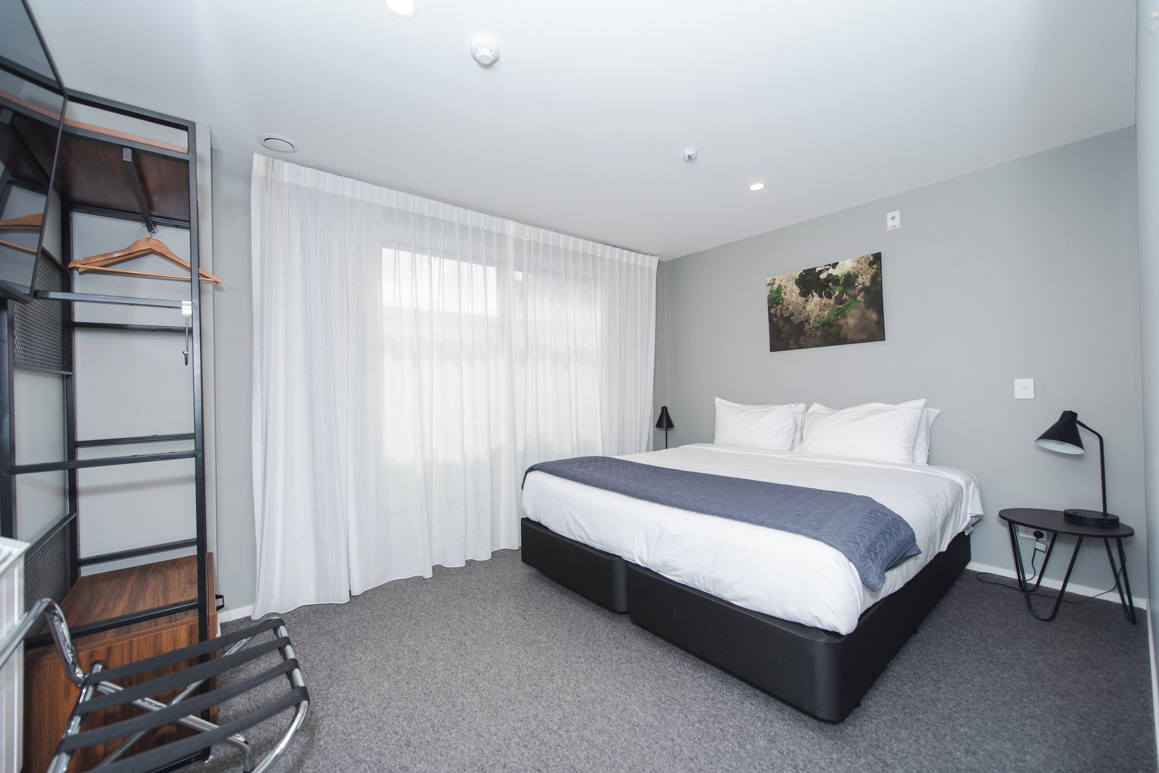 Une chambre d’hôtel moderne avec un grand lit, une armoire avec un miroir, une petite table de chevet et un tableau au mur.