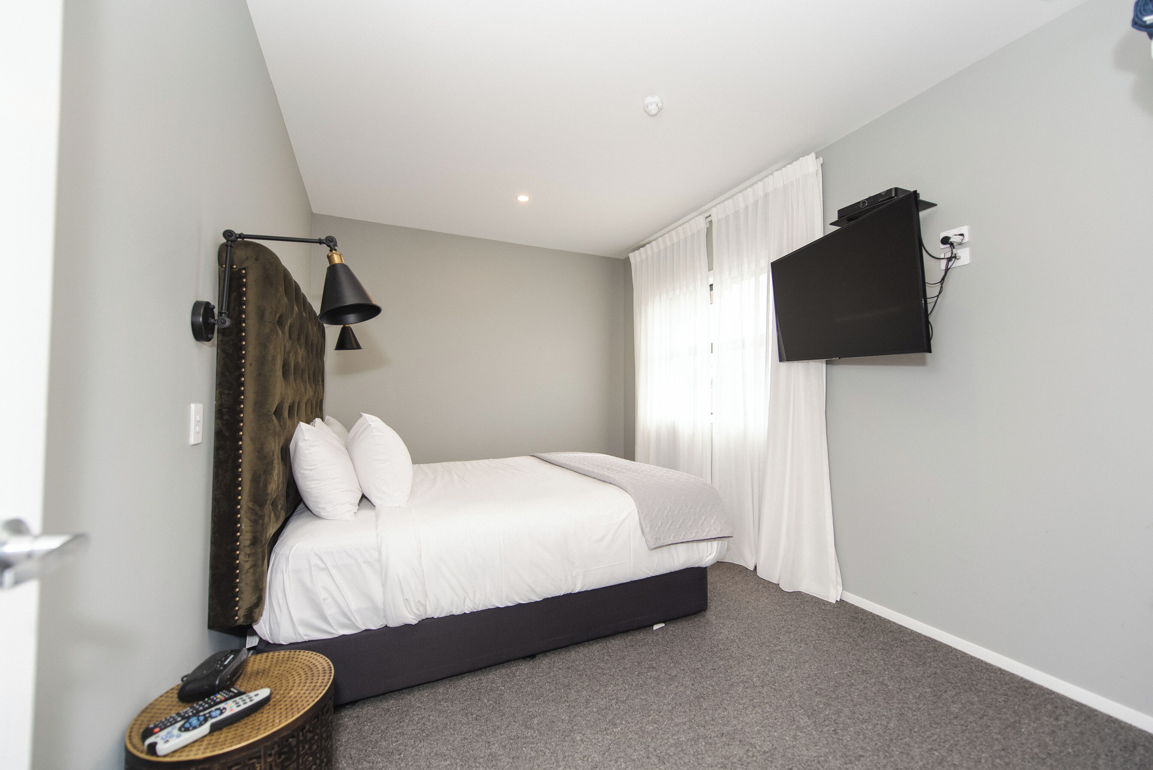 Een slaapkamer met een bed, een wandgemonteerde televisie, een lamp en een afstandsbediening op een nachtkastje.