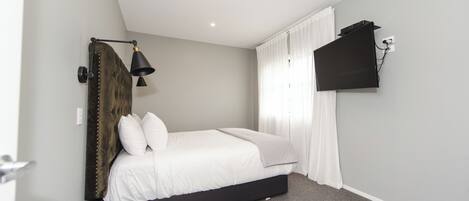 Een slaapkamer met een bed, een wandgemonteerde televisie, een lamp en een afstandsbediening op een nachtkastje.