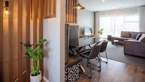 A modern living room with a sofa, a dining table with chairs, a TV, and a potted plant.