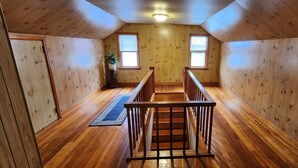 Ein Holzinnenraum mit einer zentralen Treppe, zwei Fenstern und einer Deckenleuchte.