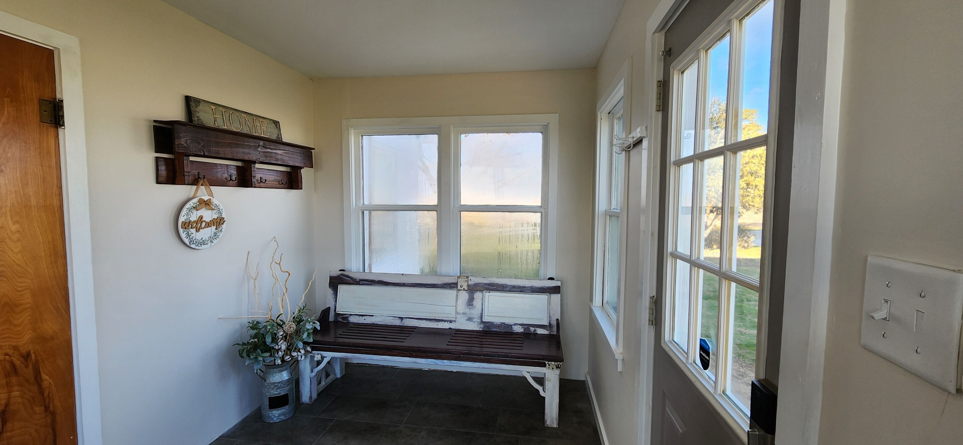 A hallway with a bench, a welcome sign, and a window with a view of the outdoors.