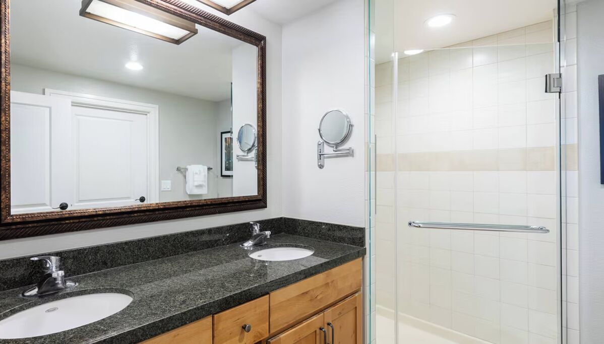 Un baño moderno con dos lavamanos, un espejo grande y una cabina de ducha de vidrio.