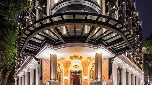 Une grande entrée d’hôtel, avec une vaste arche, un escalier menant au hall d’entrée et une façade bien éclairée.