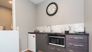 A compact kitchen with a refrigerator, microwave, and a clock on the wall. - The Residence Apartment Eight (New Plymouth)
