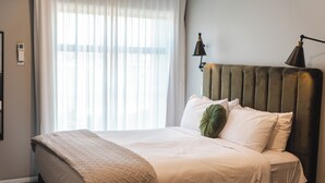 A neatly made bed with a beige quilt, a green pillow, and two bedside lamps. - The Residence Apartment Eight (New Plymouth)