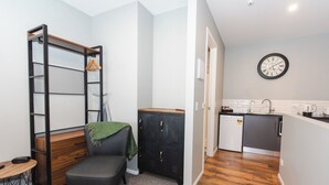 A compact living space with a kitchenette, a small dining area, and a seating area with a chair and a bench. - The Residence Apartment Eight (New Plymouth)
