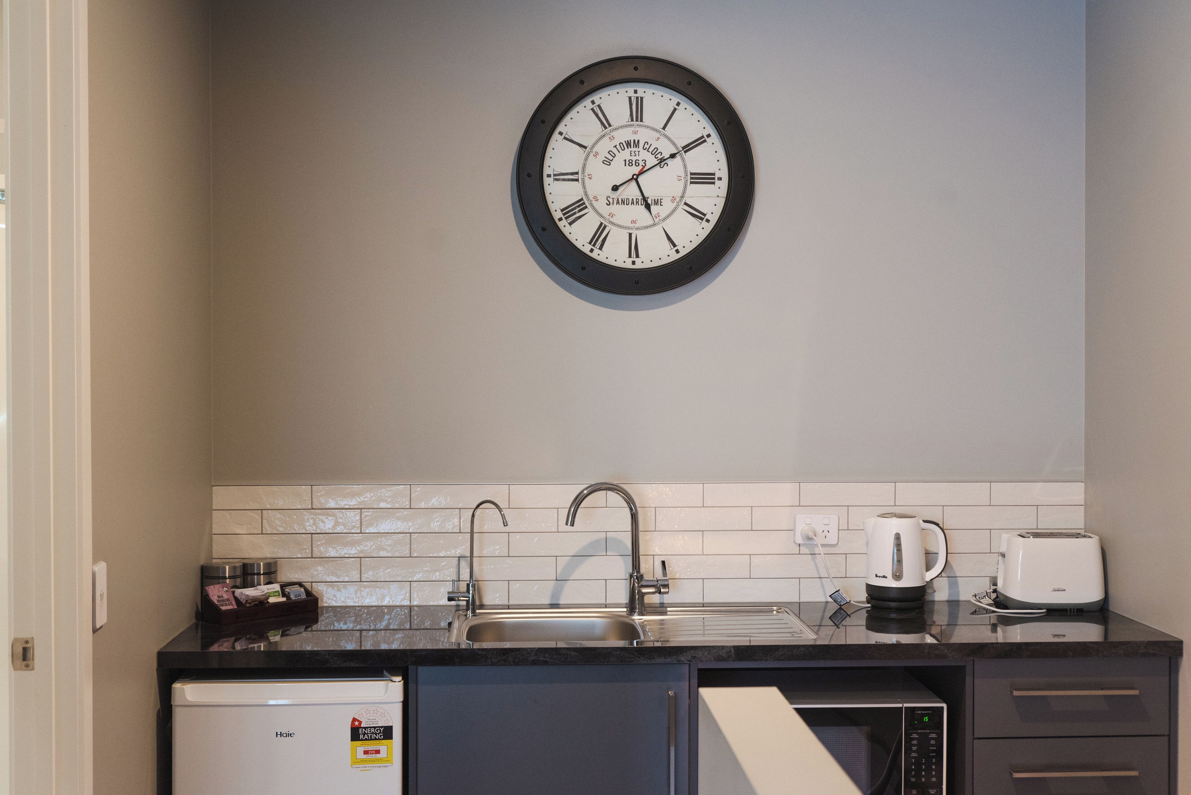 A kitchen with a clock, a sink, a coffee maker, a toaster, and a dishwasher.