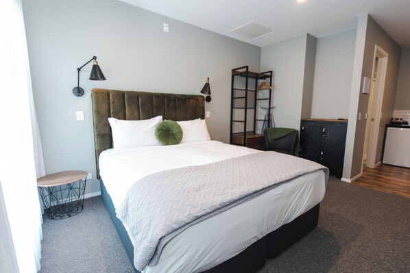 A bedroom with a large bed, a bedside table, a wardrobe, and a hanging rack. - The Residence Apartment Eight (New Plymouth)