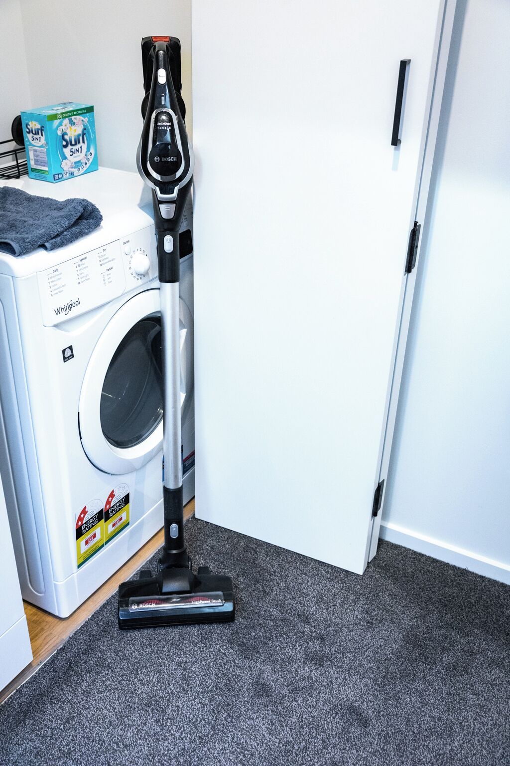 A front-loading Whirlpool washer and dryer with a Bosch upright vacuum cleaner in front.