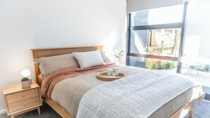Et moderne soveværelse med en træseng, et natbord og et stort vindue.