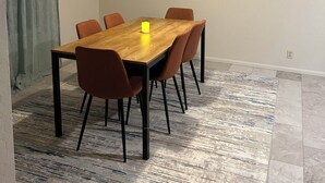 Een eetruimte met een houten tafel en zes stoelen, een hanglamp en een vloerkleed met een patroon.