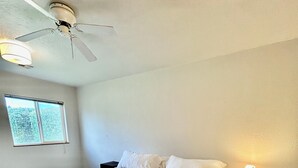 Een slaapkamer met een bed, nachtkastje, lamp, plafondventilator en raam.
