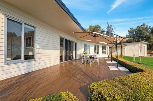 A modern house with a wooden deck, a covered patio with a table and chairs, and a small garden area.
