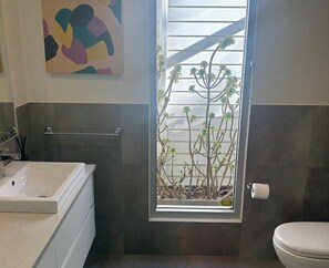 A bathroom with a white sink, a toilet, a towel rack, and a window with a view of a plant.