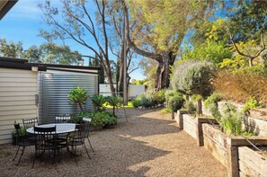 A patio with a table and chairs, surrounded by a gravel area and various plants.