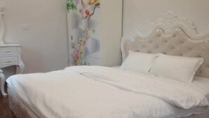 Un lit bien fait, avec du linge de lit blanc, dans une chambre dotée d’une tête de lit blanche et d’une petite table de chevet.