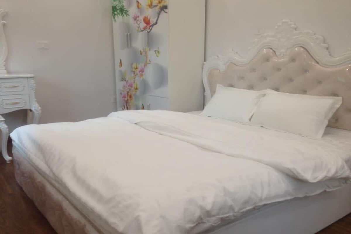 Cama bem arrumada com lençóis brancos em quarto com cabeceira branca e mesinha de cabeceira.