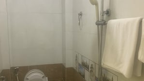 Une petite salle de bain avec des toilettes, une douche et un sol carrelé.