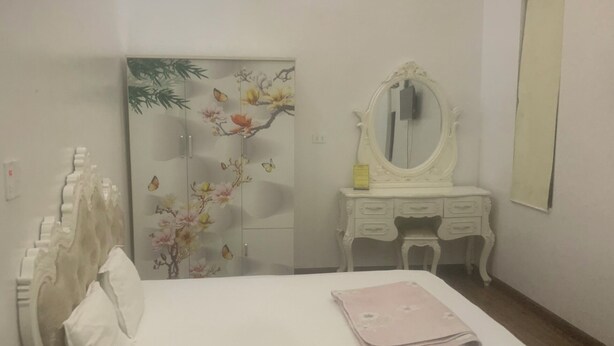 Une chambre à coucher comprenant un lit, une commode, un miroir et un mur orné d’un tableau représentant des motifs floraux.