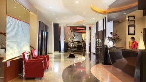 A hotel lobby with a reception desk, red seating area, and a curved floor design. - Horison Arcadia Wahid Hasyim (Jakarta)