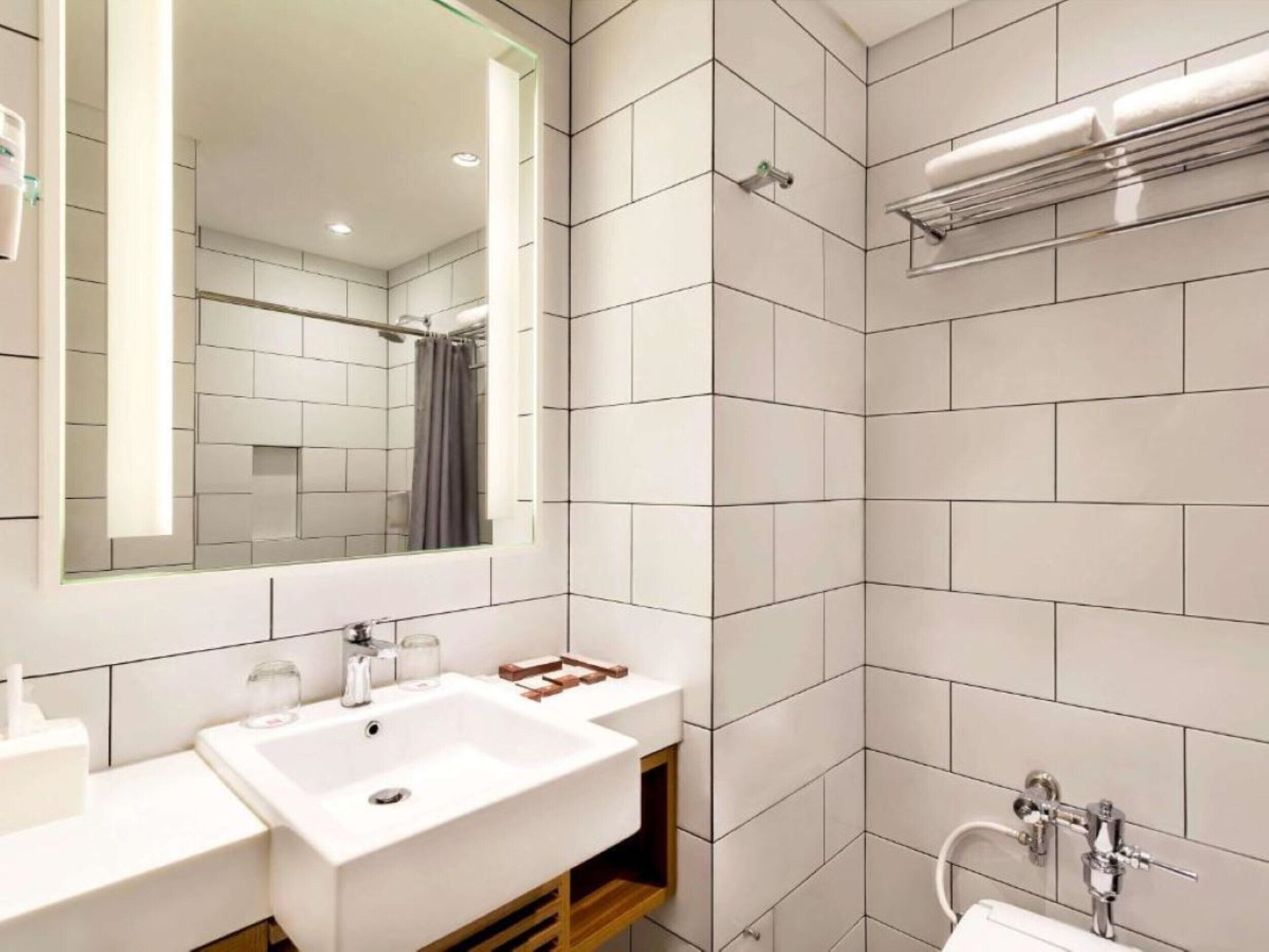 A modern bathroom with white tiles, a large mirror, a sink, and a shower area.