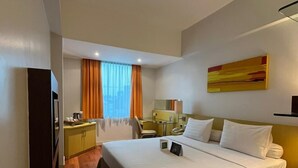 A hotel room with a large bed, a desk, a chair, a small table, a TV, and a window with curtains. - Horison Arcadia Wahid Hasyim (Jakarta)