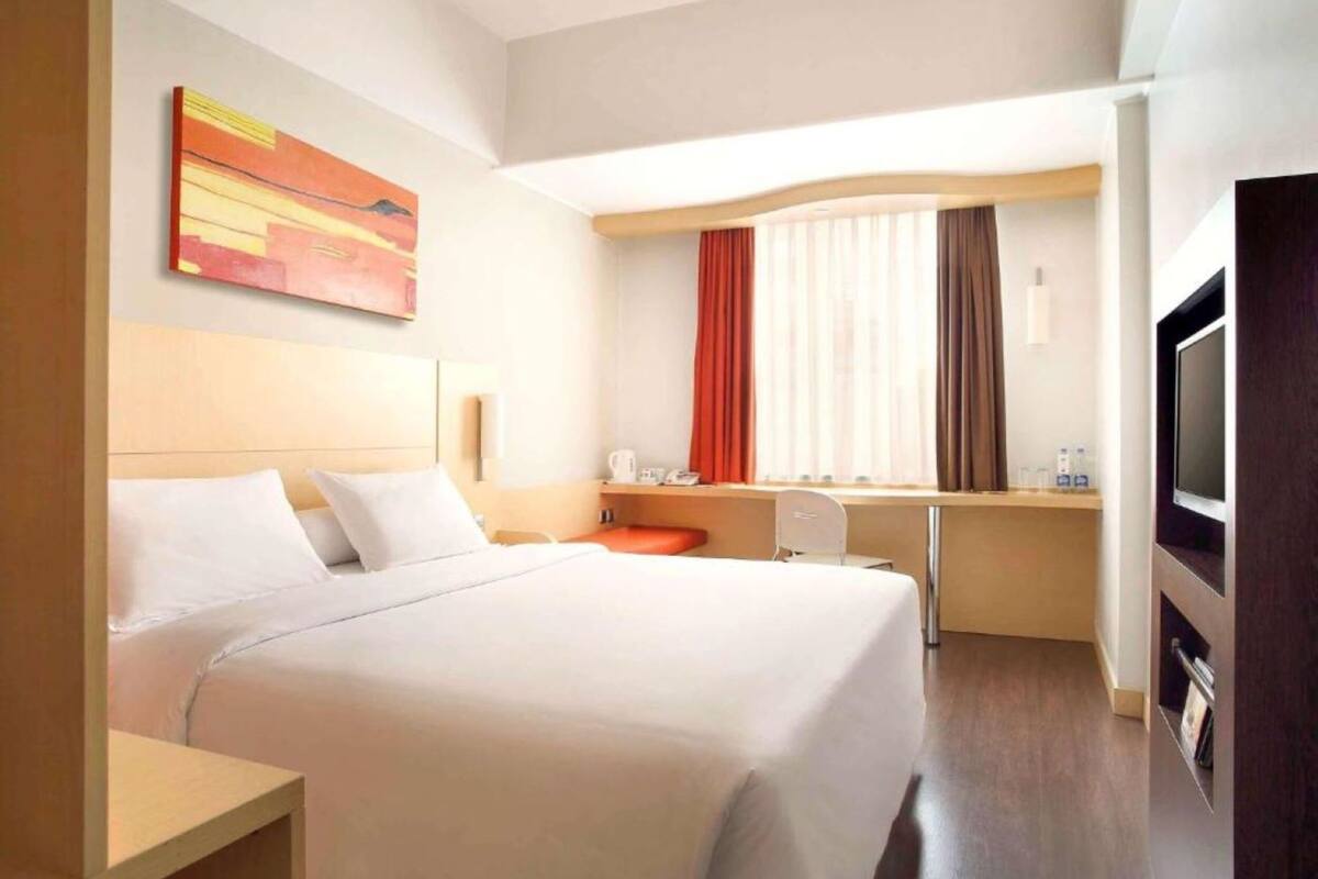 A hotel room with a large bed, a desk, a chair, a TV, and a window with curtains.