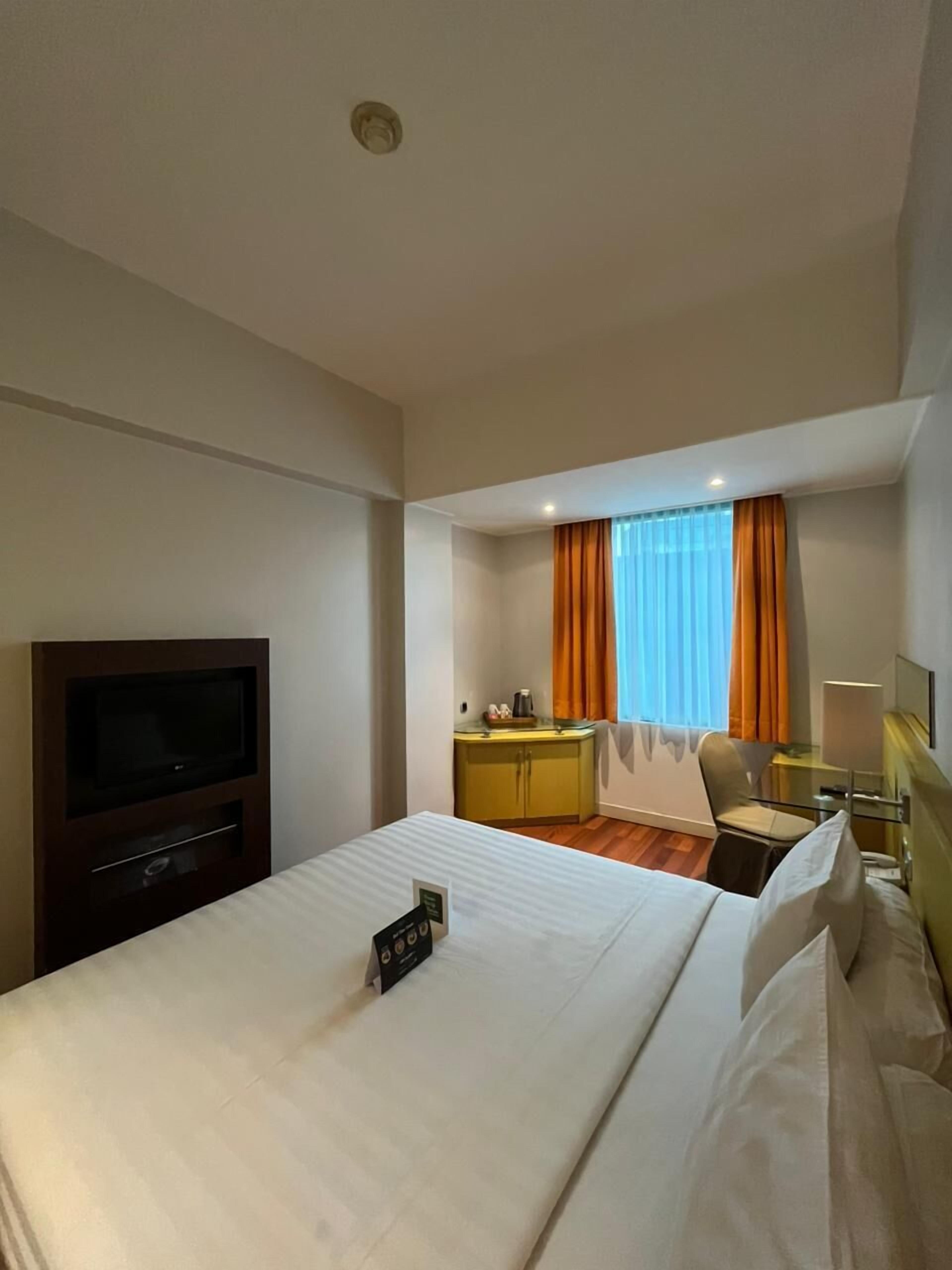 A hotel room with a large bed, a TV, a desk with a chair, and a window with curtains.