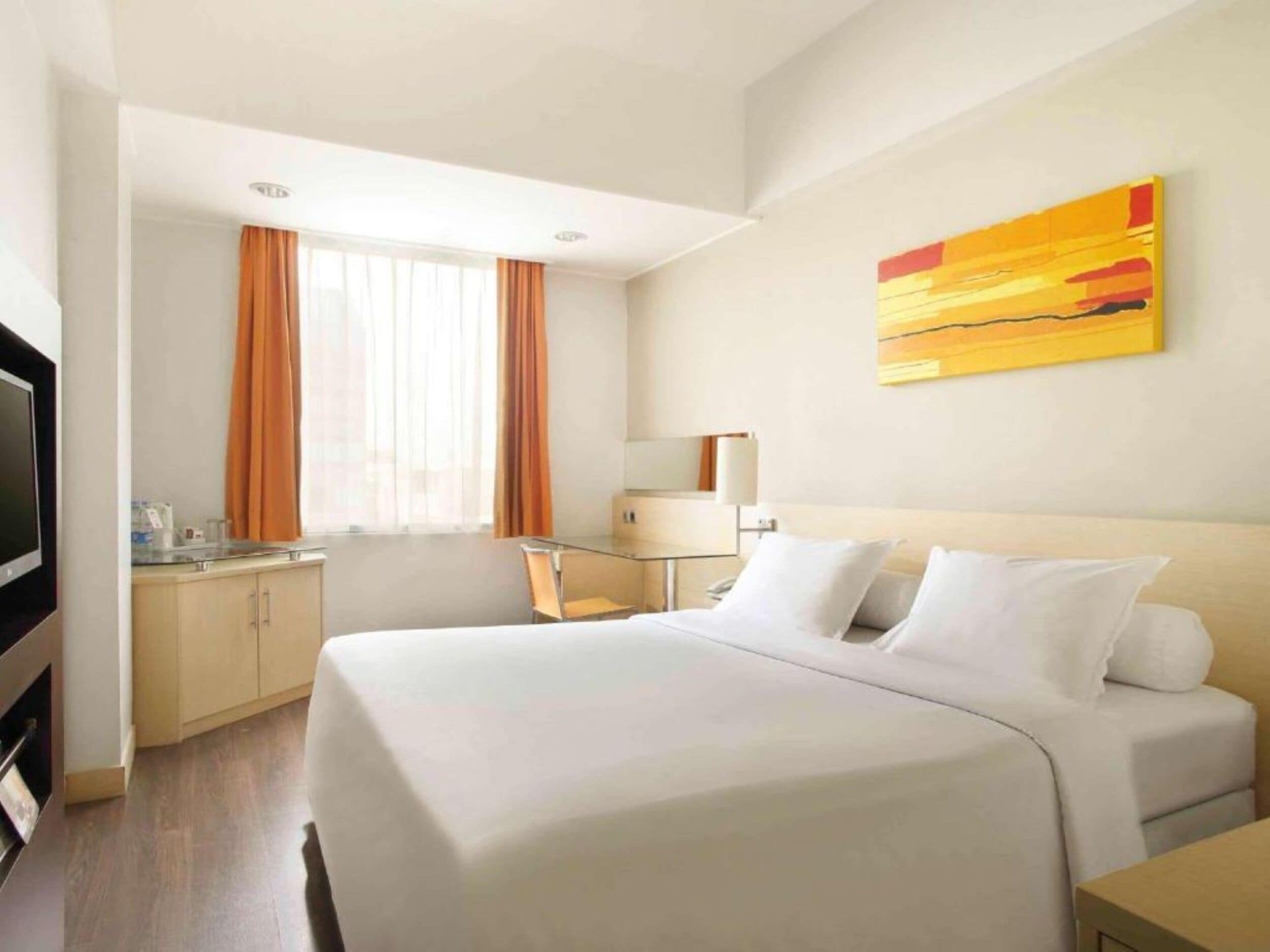 A hotel room with a large bed, a desk with a chair, a television, and a painting on the wall.