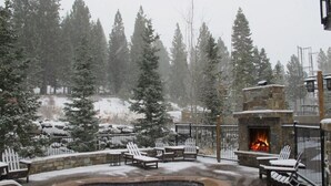 Zona de piscina exterior cubierta de nieve con sillones reclinables y una chimenea de piedra.