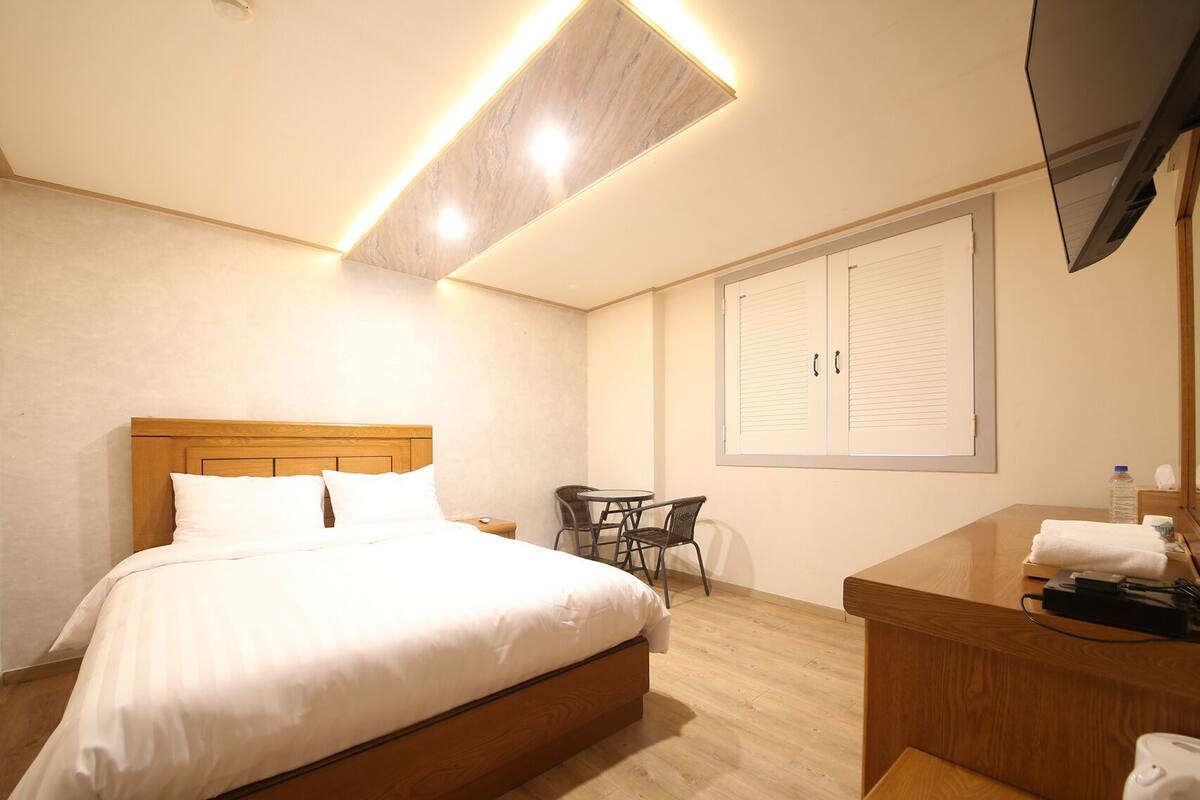 A hotel room with a large bed, a desk with a chair, a TV, and a wardrobe.