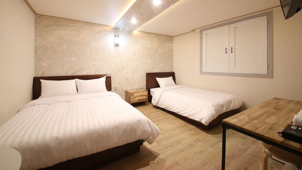 Habitación de hotel con dos camas, suelo de madera, escritorio y un mueble de pared.