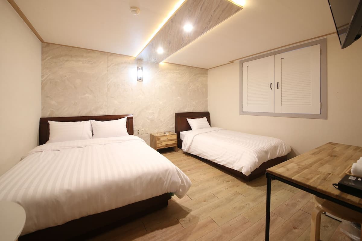 A hotel room with two beds, a wooden floor, a desk, and a wall-mounted cabinet.