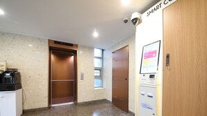 Un vestíbulo de hotel con una máquina de café, un ascensor y un quiosco informativo digital.