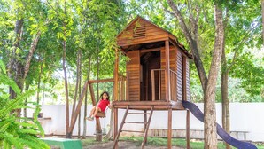 Une cabane en bois avec un toboggan, entourée d’arbres.