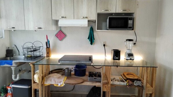 Ett kompakt kök med ett bord med glasskiva, en mikrovågsugn, en kaffebryggare och diverse köksredskap.
