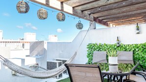 Une terrasse sur le toit agrémentée d’une pergola en bois, de guirlandes lumineuses, d’un hamac, d’une table avec des chaises et d’un mur végétal.