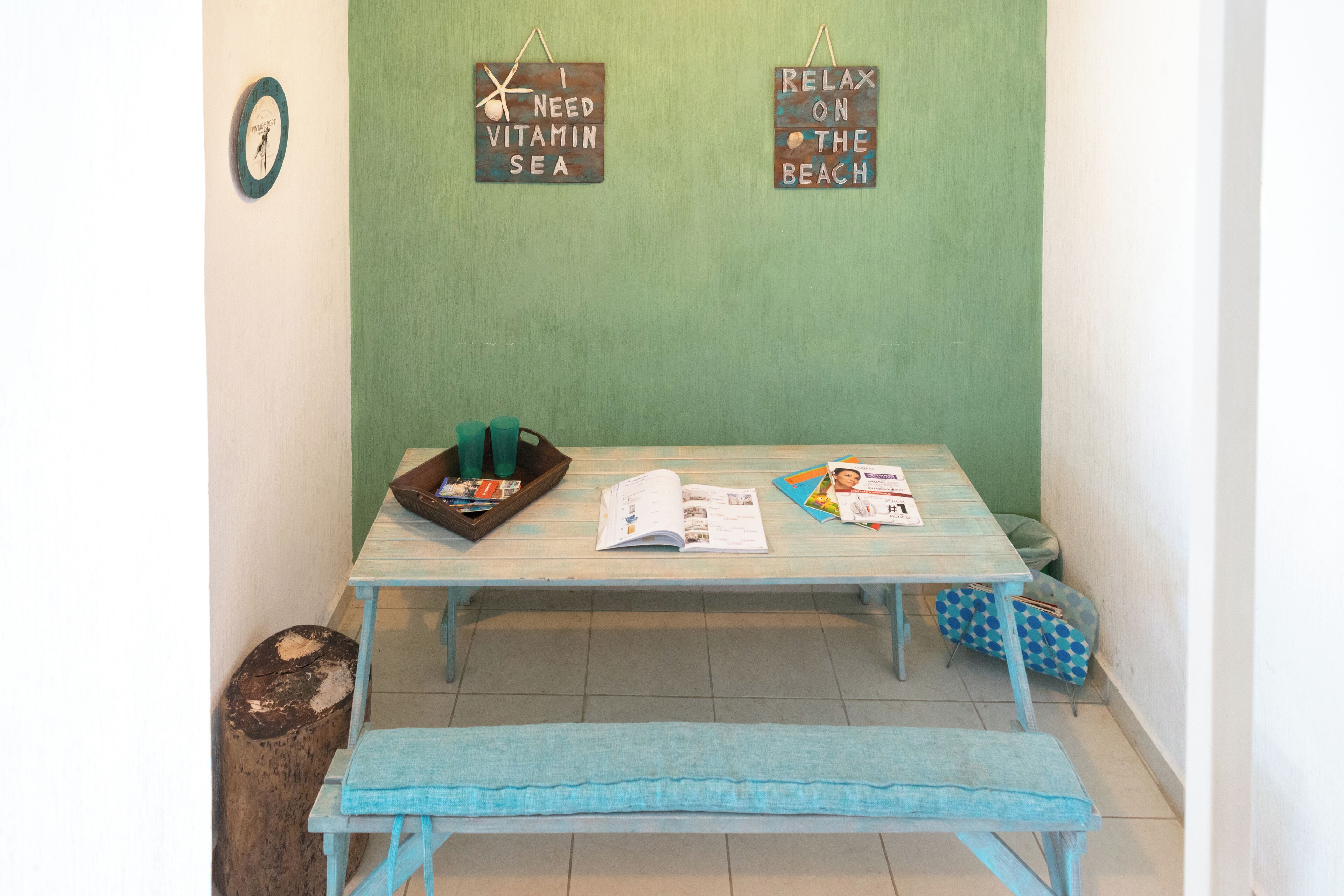 Une pièce avec un mur vert, un banc en bois, une table avec des magazines et deux panneaux accrochés au mur.