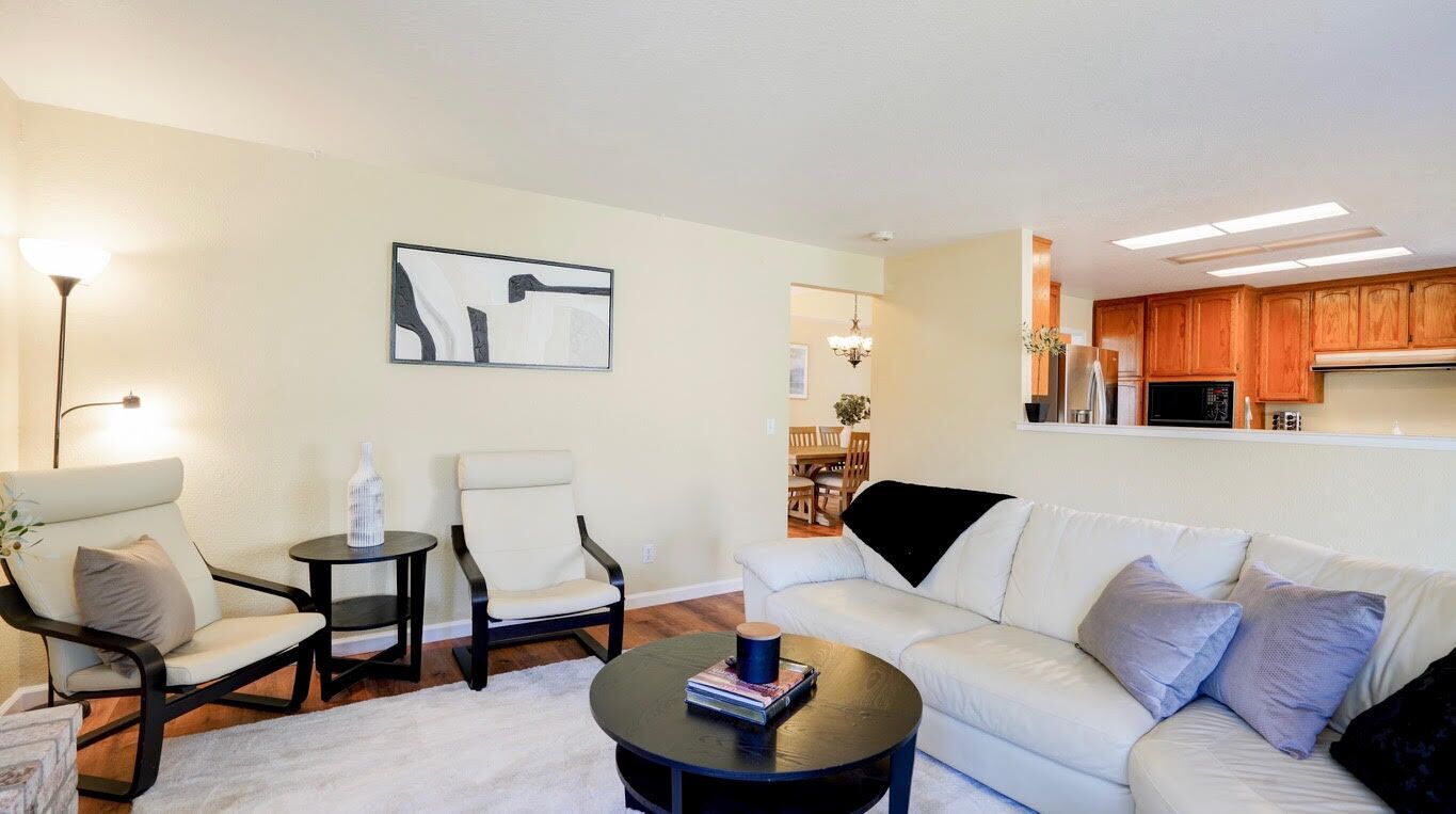 Ein Wohnzimmer mit einem weißen Sofa, zwei Sesseln, einem Couchtisch und einem Gemälde an der Wand.