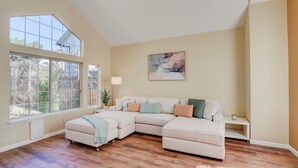 A living room with a sectional sofa, a large window, and a painting on the wall. - SUNNY SPACIOUS RETREAT NEAR GOLF COURSE W/ HOT TUB - WINE COUNTRY GETAWAY  (Windsor)