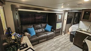 A compact living space with a leather couch, a small kitchenette, and a map on the wall. - RV in Art District and Close to the BEACH! Pool & Hot-Tub & Fenced/Pet-Friendly! (Melbourne)