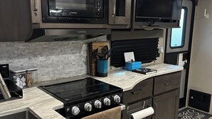 A compact kitchen with a stove, microwave, and oven, a small sink, and a window. - RV in Art District and Close to the BEACH! Pool & Hot-Tub & Fenced/Pet-Friendly! (Melbourne)