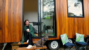 Une personne assise sur un banc devant une cabane en bois, avec un chien, une porte coulissante et une petite table.