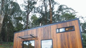 Une cabane moderne en bois, dotée d’une porte coulissante, d’une petite fenêtre et d’un escalier menant à l’entrée.