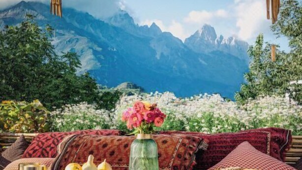 Ein gemütlicher Sitzbereich im Freien mit einem Holztisch, Kissen und einem Blumenstrauß.