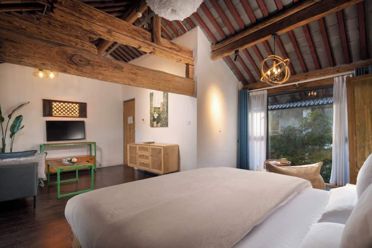 Amplia habitación con cama grande, vigas de madera, televisión y vistas a zonas verdes.