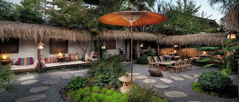 A traditional-style outdoor seating area with thatched roofs, stone pathways, and a central decorative lantern.